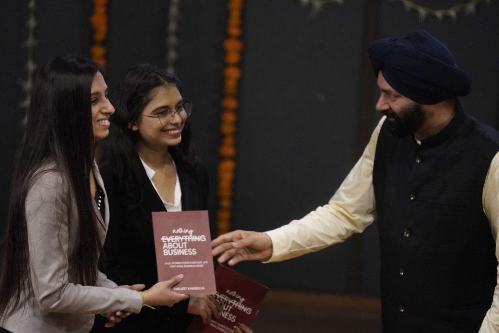 Harjeet handing a copy of Nothing About Business to young readers