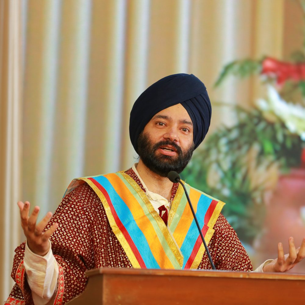 Harjeet speaking at a podium wearing a ceremonial stole